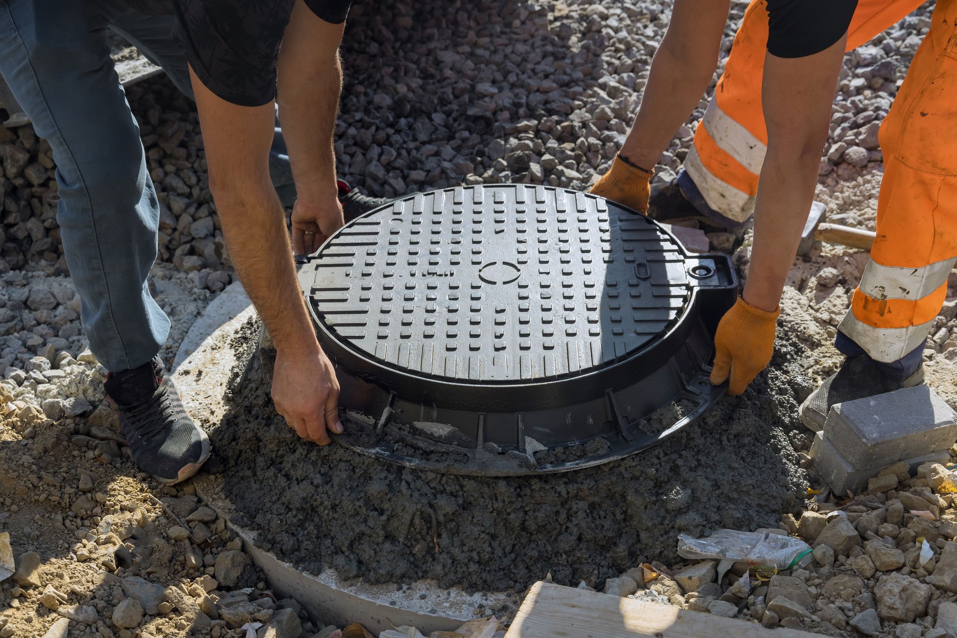 A cast iron sewer hatch is being installed in a concrete well, in preparation for the installation of a water sewer well in the ground.