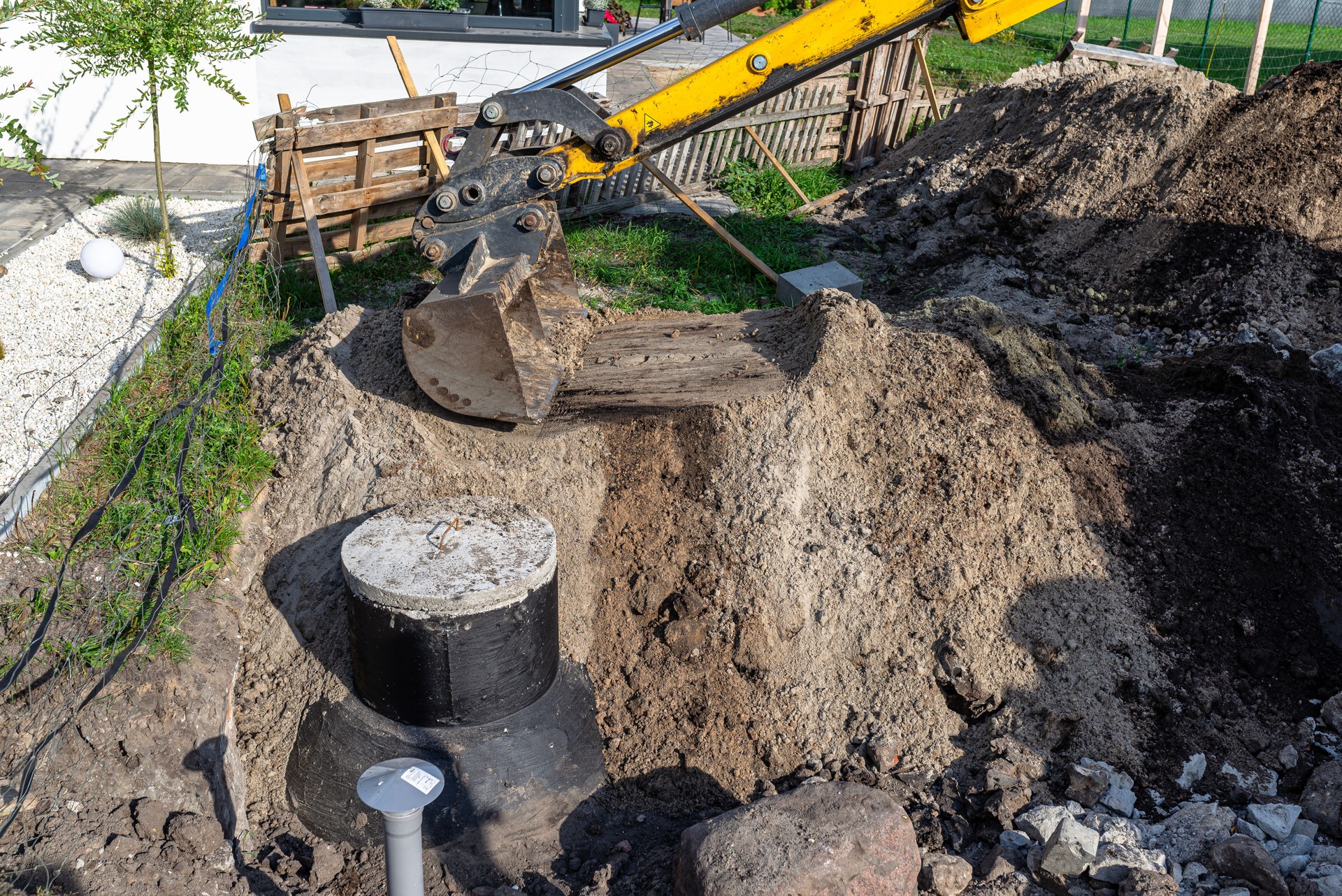 Using an excavator to bury a 10 m3 concrete septic tank located in the garden next to the house.